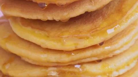 Syrup being poured onto stack of steaming pancakes on pink background. Видео 336589275