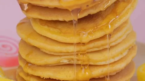 Syrup pouring on to stack of pancakes with pink background, closeup. Stock-Footage 336589274