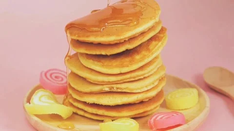 Syrup pouring on to stack of pancakes with pink background, closeup. Stock-Footage 336589283