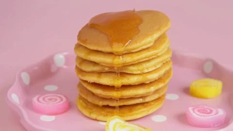 Syrup pouring on to stack of pancakes with pink background, closeup. Stock-Footage 336589289