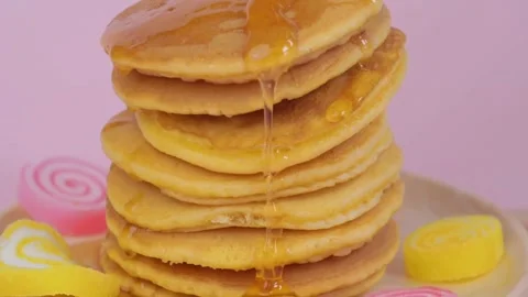 Syrup pouring on to stack of pancakes with pink background, closeup. Stock-Footage 336589300