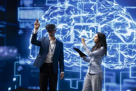 System administrator wearing VR headset looking at hologram next to coworker Stock Photos