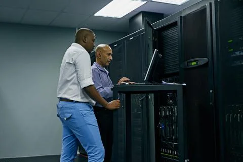 System administrators to the rescue. two IT technicians using a computer while Stock Photos