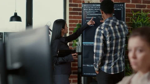 System developers analyzing code on wall screen tv looking for errors comparing Stock Footage 168238667