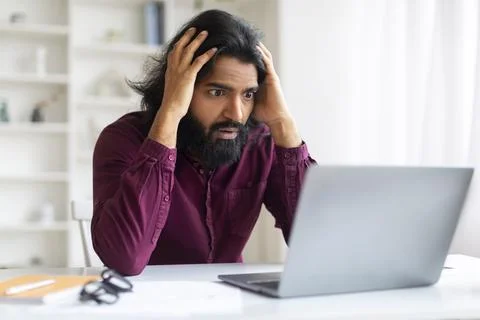 System Error. Shocked indian man looking at laptop screen and touching head Stock Photos