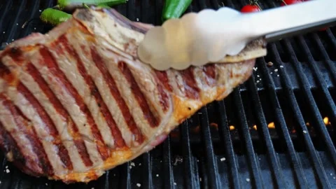 T bone beef steak on grill grate, flame. Turn steak over. Close up. Slow motion Video stock 255826062