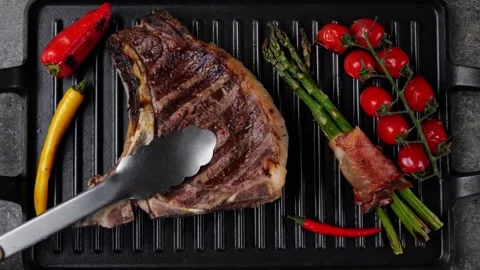 T- bone beef steak  vegetables on grill pan. Steak turning over on the grill. Stock Footage 273219282