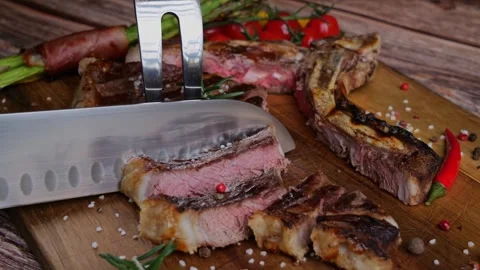 T- bone steak grill cut into pieces with  knife on  cutting board.  Slow motion Stock Footage 273219149