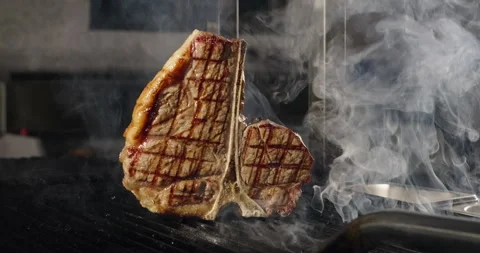 T-bone steak grilling on barbecue charcoal grill in smoke. Grilling BBQ meat Stock Footage 270384615