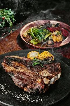 T-Bone steak serving with grilled vegetables on a black round plate on a Stock Photos