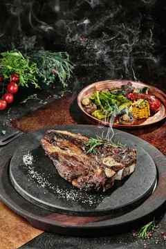 T-Bone steak serving with grilled vegetables on a black round plate on a Stock Photos