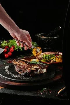 T-Bone steak serving with grilled vegetables on a black round plate on a Stock Photos