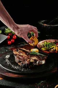 T-Bone steak serving with grilled vegetables on a black round plate on a Stock Photos