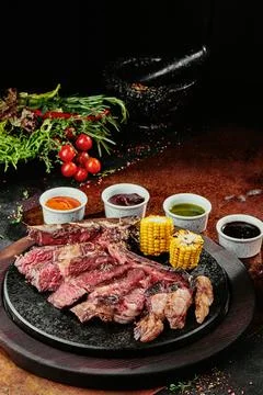 T-Bone Steak serving with grilled vegetables and various sauces on a black round Stock Photos