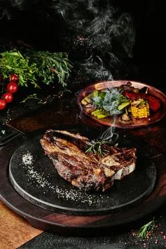 T-Bone steak serving with grilled vegetables on a black round plate on a Stock Photos