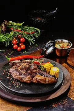 T-Bone steak serving with grilled vegetables on a black round plate on a Stock Photos