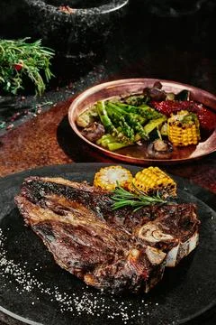 T-Bone steak serving with grilled vegetables on a black round plate on a Stock Photos