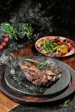 T-Bone steak serving with grilled vegetables on a black round plate on a Stock Photos