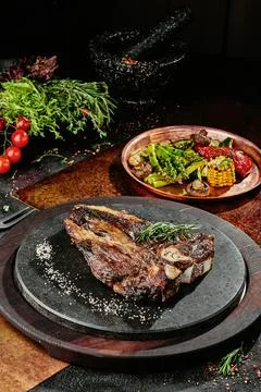 T-Bone steak serving with grilled vegetables on a black round plate on a Stock Photos