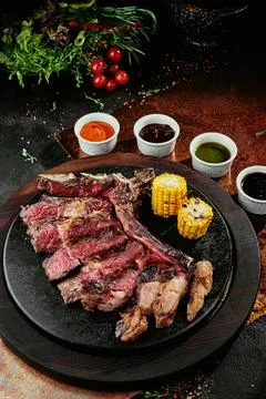 T-Bone Steak serving with grilled vegetables and various sauces on a black round Stock Photos