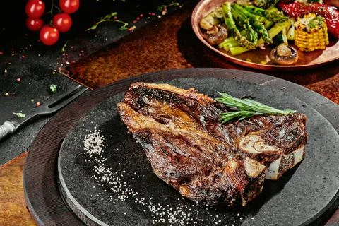 T-Bone steak serving with grilled vegetables on a black round plate on a Stock Photos