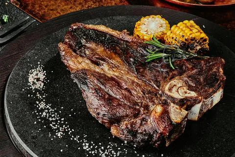 T-Bone steak serving with grilled vegetables on a black round plate on a Stock Photos