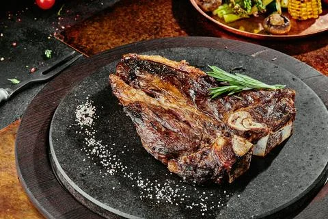 T-Bone steak serving with grilled vegetables on a black round plate on a Stock-Fotos