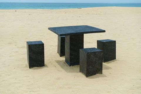 A table and chairs made of stone stands on seashore Stock Photos