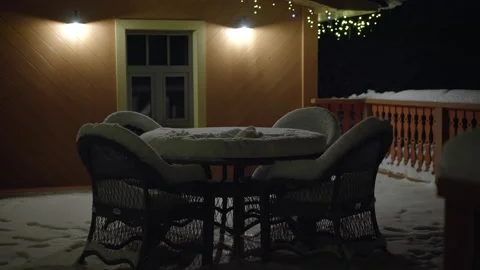 Table and chairs stand outside covered with snow at night Stock Footage 236014629