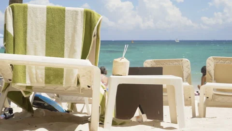 Table and chaise lounge on the beach. coconut with a straw against the Stock Footage 108516184