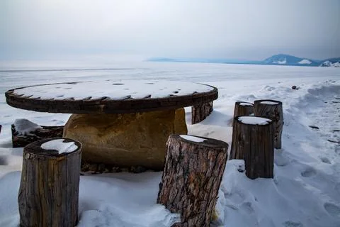 A table and stools are in the snow, with mountains behind Stock Photos