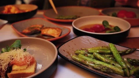 On the table are Asian fish dishes and fried asparagus. Close-up: a hand picking Stock Footage 326199355