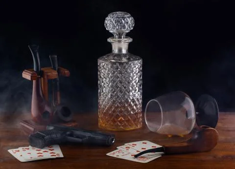 On the table are playing cards a pistol Smoking pipes and an overturned glass Stock Photos