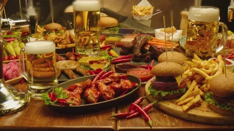 Table with beer fast food fried fries chicken wings burgers sausages , sauces Stock Footage 213579953