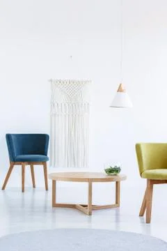 Table between blue and yellow armchair in white living room interior with lam Stock Photos