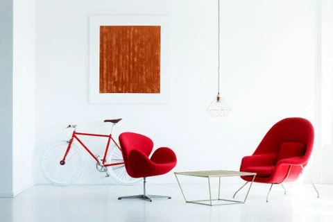 Table between red armchairs in white living room interior with bicycle and pa Stock Photos