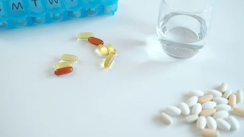 On the table is a blue pill boxes, yellow capsules and glass of water Stock Footage 73226455