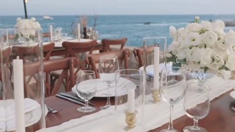 Table with a bouquet of white roses, wine glasses, plates and candles by the sea Stock-Footage 280445945