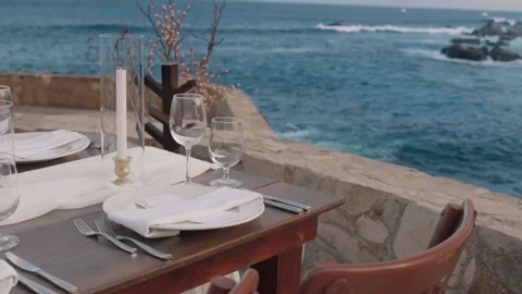 Table with a bouquet of white roses, wine glasses, plates and candles by the sea Stock-Footage 280445997
