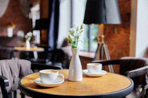A table in a cafe, two white cups of coffee and a vase with a bouquet of flowers Stock Photos