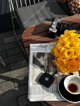 A table with a camera, newspaper, and flowers on it. Stock Photos