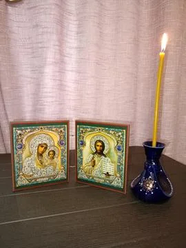 On the table is a candlestick with a burning candle and a pair of Orthodox .. Stock Photos