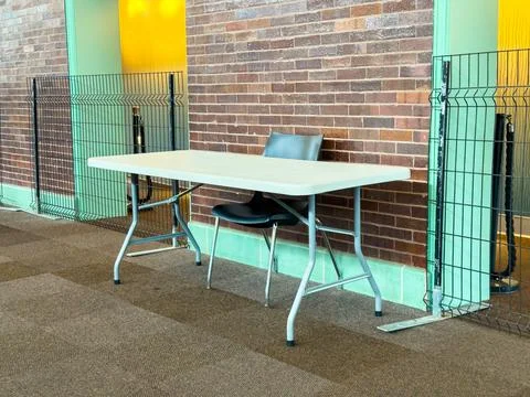 A table with a chair is positioned next to a brick wall. Metal fences surroun Fotos de archivo