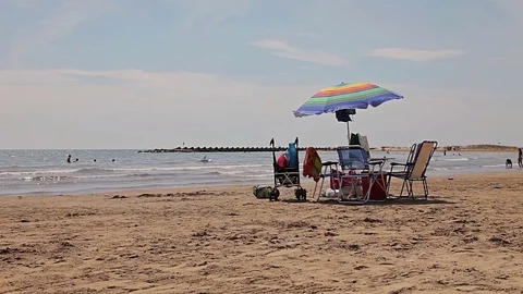 A table with chairs protected by an umbrella. Spanish beaches in Catalonia. Stock Footage 75557322