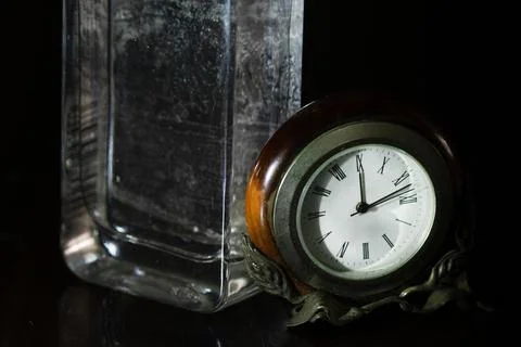 Table clock and glass bottle on dark background Stock Photos