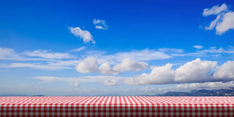 Table covered with red checkered tablecloth on blue sky background, copy spac Ilustração Stock