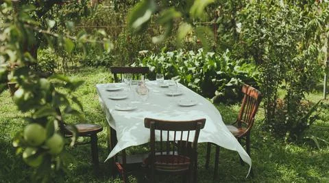 Table covered with a white tablecloth stands in the garden. Stock Photos