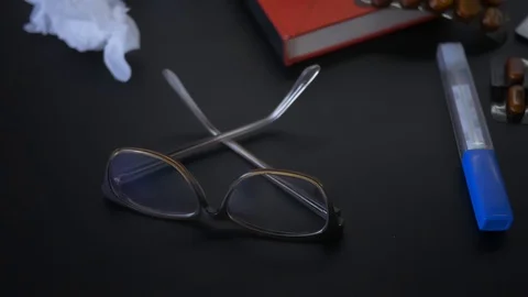 Table with cup of tea, pills, nose spray, glasses, book, thermometer, drugs b 스톡 동영상 119820111