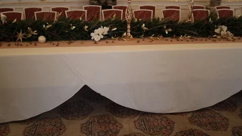 A table decorated with a festive garland of greenery, white flowers, and gold ac Stock Footage 294771952