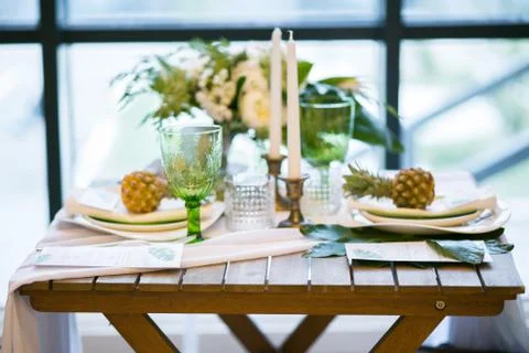 Table decorated with plates, pineapples, candles and flowers, green and white Stock Photos